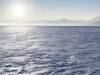 a snow - covered ocean with mountains in the distance and one boat floating near it