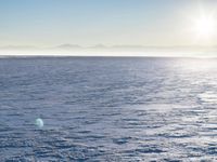 a snow - covered ocean with mountains in the distance and one boat floating near it
