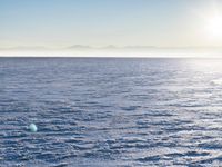 a snow - covered ocean with mountains in the distance and one boat floating near it
