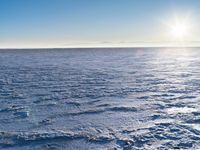 a snow - covered ocean with mountains in the distance and one boat floating near it
