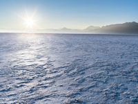a snow - covered ocean with mountains in the distance and one boat floating near it