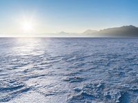 a snow - covered ocean with mountains in the distance and one boat floating near it