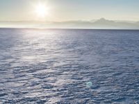 a snow - covered ocean with mountains in the distance and one boat floating near it
