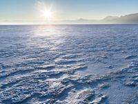 a snow - covered ocean with mountains in the distance and one boat floating near it