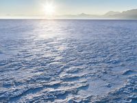 a snow - covered ocean with mountains in the distance and one boat floating near it