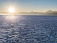 a snow - covered ocean with mountains in the distance and one boat floating near it