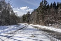 a long road with snow and trees on both sides with sky and clouds above them