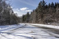 a long road with snow and trees on both sides with sky and clouds above them