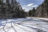 a long road with snow and trees on both sides with sky and clouds above them