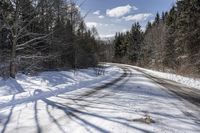 a long road with snow and trees on both sides with sky and clouds above them