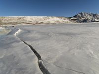a snow covered plain has a crack in the ice that has been washed off the ground