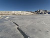 a snow covered plain has a crack in the ice that has been washed off the ground