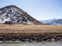 a small stone building on top of a snow covered hill next to a body of water