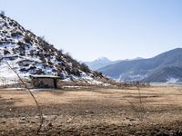 a small stone building on top of a snow covered hill next to a body of water