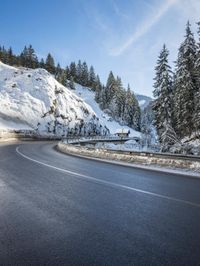 road in the mountains with snow on it and evergreen trees on both sides with sunbeams and blue skies