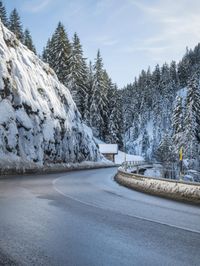 road in the mountains with snow on it and evergreen trees on both sides with sunbeams and blue skies