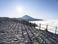 a fence with the top of it covered in snow next to a mountain with some clouds