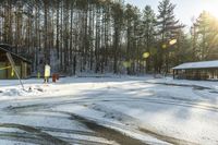 a small building and some trees in the back ground covered in snow and the sun