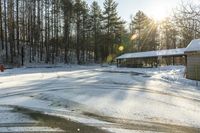 a small building and some trees in the back ground covered in snow and the sun