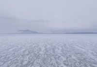 a picture of an overcast sky over a vast plain of snow with a large mountain in the distance