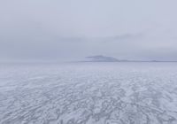 a picture of an overcast sky over a vast plain of snow with a large mountain in the distance