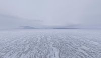 a picture of an overcast sky over a vast plain of snow with a large mountain in the distance