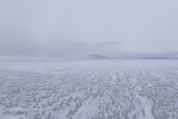 a picture of an overcast sky over a vast plain of snow with a large mountain in the distance