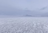 a picture of an overcast sky over a vast plain of snow with a large mountain in the distance