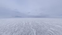 a picture of an overcast sky over a vast plain of snow with a large mountain in the distance