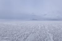 a picture of an overcast sky over a vast plain of snow with a large mountain in the distance