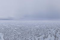 a snow covered field with an ocean of frozen water and hills in the background is a cloudy sky