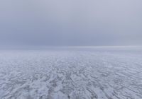 a snow covered field with an ocean of frozen water and hills in the background is a cloudy sky