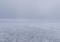 a snow covered field with an ocean of frozen water and hills in the background is a cloudy sky