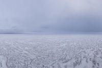 a snow covered field with an ocean of frozen water and hills in the background is a cloudy sky