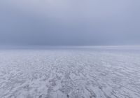 a snow covered field with an ocean of frozen water and hills in the background is a cloudy sky