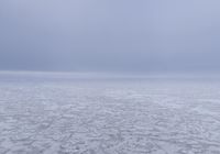 a snow covered field with an ocean of frozen water and hills in the background is a cloudy sky