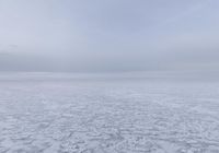 a snow covered field with an ocean of frozen water and hills in the background is a cloudy sky