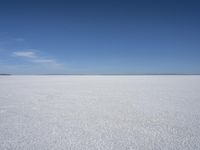 a blue sky above a vast snowy landscape with footprints on the snow floor of a salt flat area