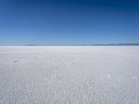 a blue sky above a vast snowy landscape with footprints on the snow floor of a salt flat area