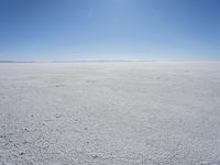 a blue sky above a vast snowy landscape with footprints on the snow floor of a salt flat area