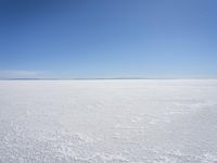 a blue sky above a vast snowy landscape with footprints on the snow floor of a salt flat area