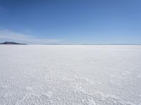 a blue sky above a vast snowy landscape with footprints on the snow floor of a salt flat area