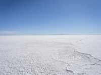 a blue sky above a vast snowy landscape with footprints on the snow floor of a salt flat area