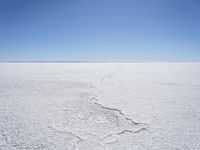 a blue sky above a vast snowy landscape with footprints on the snow floor of a salt flat area