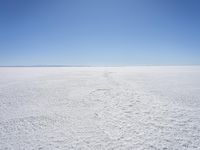 a blue sky above a vast snowy landscape with footprints on the snow floor of a salt flat area