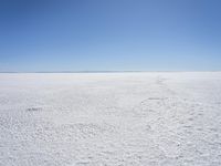 a blue sky above a vast snowy landscape with footprints on the snow floor of a salt flat area