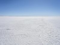 a blue sky above a vast snowy landscape with footprints on the snow floor of a salt flat area