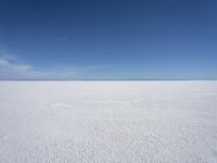 a blue sky above a vast snowy landscape with footprints on the snow floor of a salt flat area