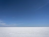 a blue sky above a vast snowy landscape with footprints on the snow floor of a salt flat area