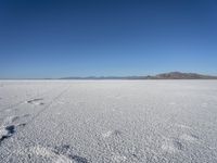 a lone snow field with a mountain in the distance and a person walking on the snow, leaving footprints